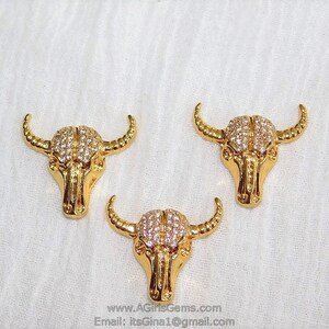 May include: Three gold-tone bull head charms with clear rhinestone accents.