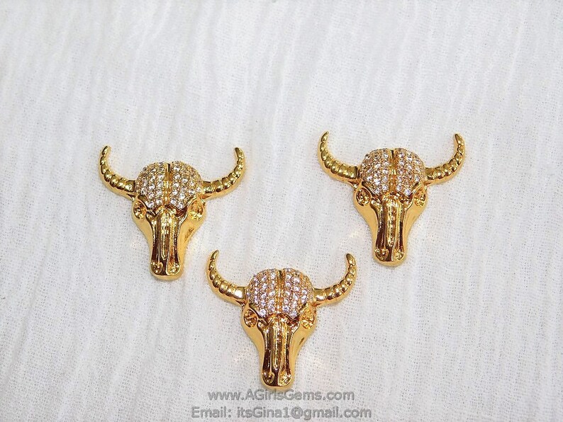 May include: Three gold-tone bull head charms with clear rhinestone accents.