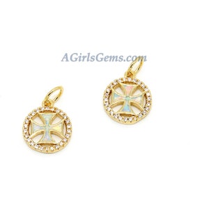 May include: Two gold-colored pendants with a cross design. Each pendant features a cross shape with a colorful opal-like center, surrounded by a circle of small, clear gemstones. The pendants have a loop at the top for a chain. The website address AGirlsGems.com is visible.