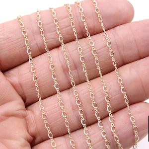 May include: A close-up of a gold chain necklace. The chain is made of small, oval-shaped links. The chain is lying on a hand, and the background is white.