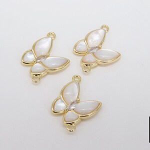 May include: Three gold butterfly charms with white mother of pearl wings and clear rhinestone accents. The charms have a loop on the top for attaching to jewelry.