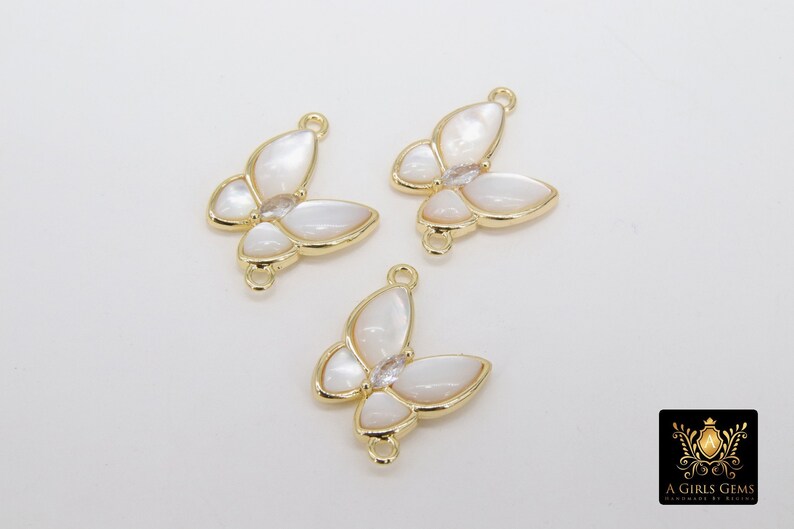 May include: Three gold butterfly charms with white mother of pearl wings and clear rhinestone accents. The charms have a loop on the top for attaching to jewelry.