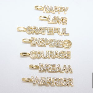 May include: Seven gold charms with diamond-like accents spelling out the words "Happy", "Love", "Grateful", "Inspired", "Courage", "Dream", and "Warrior".