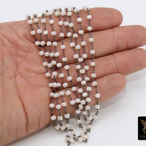 May include: A strand of white faceted beads strung on a black chain. The beads are small and round, and the chain is delicate. The strand is about 18 inches long.