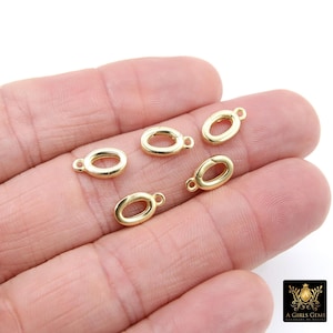 May include: Five gold-colored oval-shaped jewelry clasps with small loops. The clasps are displayed on a light-colored background. The clasps are likely used for necklaces or bracelets. The image includes the logo for "A Girls Gems".