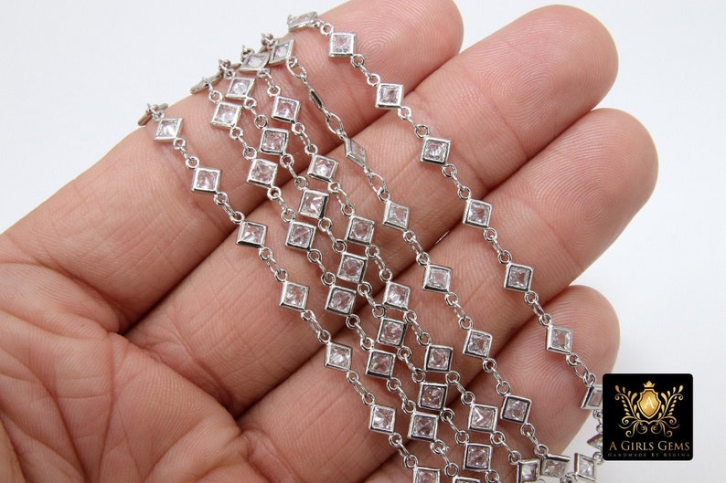 K&ouml;nnte beinhalten: Eine silberne Kette mit quadratischen, klaren Kristallen. Die Kette liegt auf einer Hand und zeigt die Details der Kette.