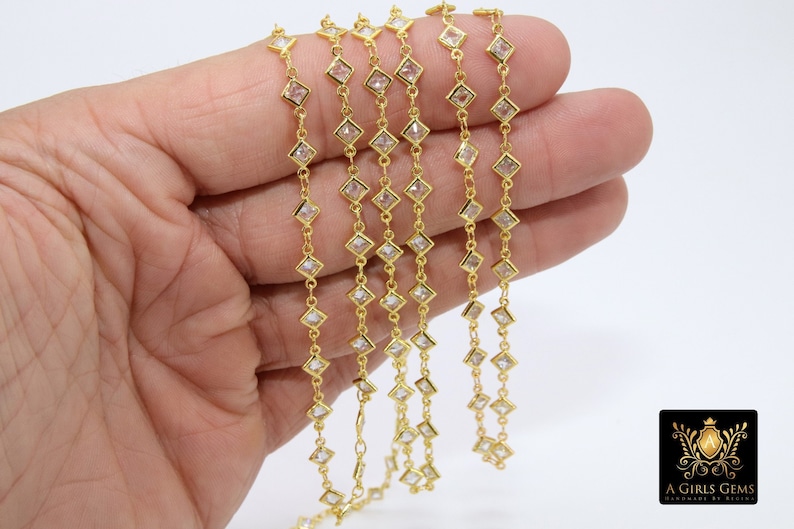 K&ouml;nnte beinhalten: Goldkette mit quadratischen, klaren Steinen. Die Kette wird in einer Hand gezeigt, mit mehreren Str&auml;ngen der Kette.