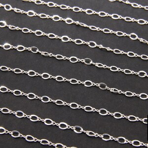 May include: A silver chain with oval links. The chain is laid out in rows on a black background.