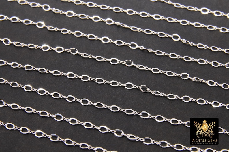 May include: A silver chain with oval links. The chain is laid out in rows on a black background.