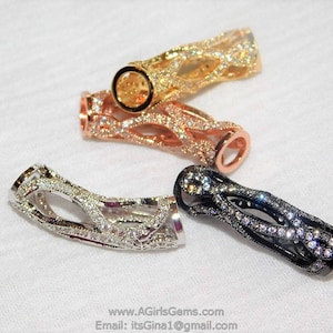 May include: Four decorative jewelry clasps in gold, rose gold, silver, and black. Each clasp features an openwork design and is encrusted with small, sparkling gemstones. The clasps are displayed on a white surface.