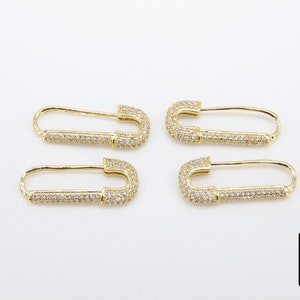 May include: Four gold safety pin earrings with clear cubic zirconia stones. The earrings are a popular style of jewelry.