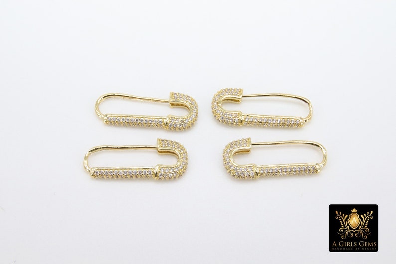 May include: Four gold safety pin earrings with clear cubic zirconia stones. The earrings are a popular style of jewelry.