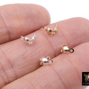 May include: Close-up of several small jewelry findings in gold and silver tones. The findings have a decorative shape with a loop for attaching to other jewelry components. The items are displayed on a person's hand.