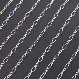 May include: Multiple strands of silver chain with oval links. The chains are arranged in parallel lines on a black background.