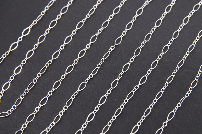 May include: Multiple strands of silver chain with oval links. The chains are arranged in parallel lines on a black background.