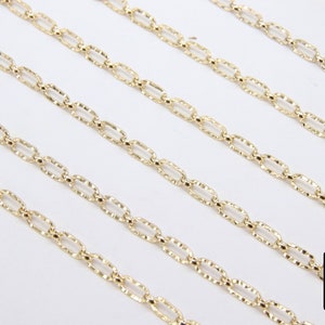 May include: Five gold chains with a textured, oval-shaped link design. The chains are laid out in parallel lines on a white surface.