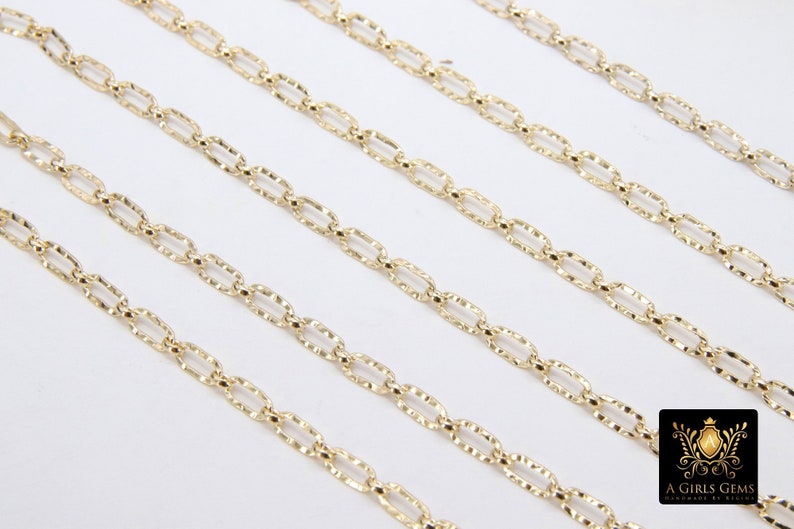 May include: Five gold chains with a textured, oval-shaped link design. The chains are laid out in parallel lines on a white surface.