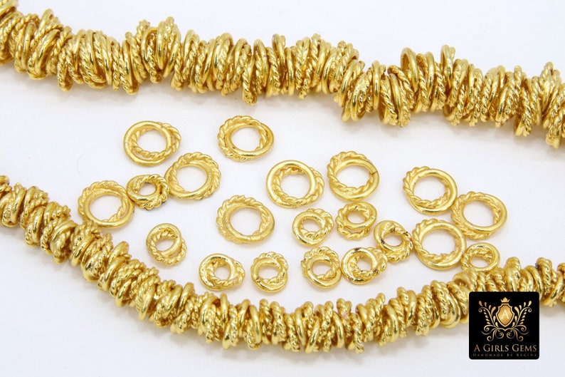 Pu&ograve; includere: Anelli di salto in metallo dorato con una texture a corda. Gli anelli sono sparsi su una superficie bianca. A Girls Gems &egrave; stampato nell'angolo in basso a destra dell'immagine.