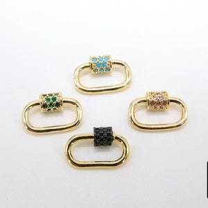 May include: Four gold-colored oval carabiner clasps with different colored gem accents. One clasp has turquoise gems, one has green gems, one has pink gems, and one has black gems. The clasps are on a white background.