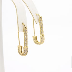 May include: A pair of gold safety pin earrings with clear cubic zirconia stones.