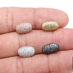 May include: Four oval-shaped beads with a pave setting of clear cubic zirconia stones. The beads are in different metal finishes: rose gold, gold, silver, and black.