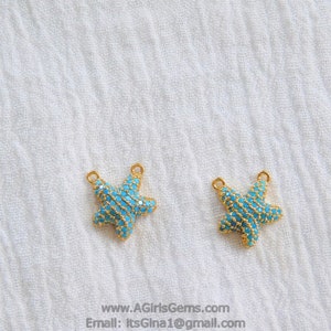 Pode incluir: Dois pingentes de estrela do mar dourados com detalhes em cristal azul. Os pingentes têm dois anéis de salto para prender em joias.
