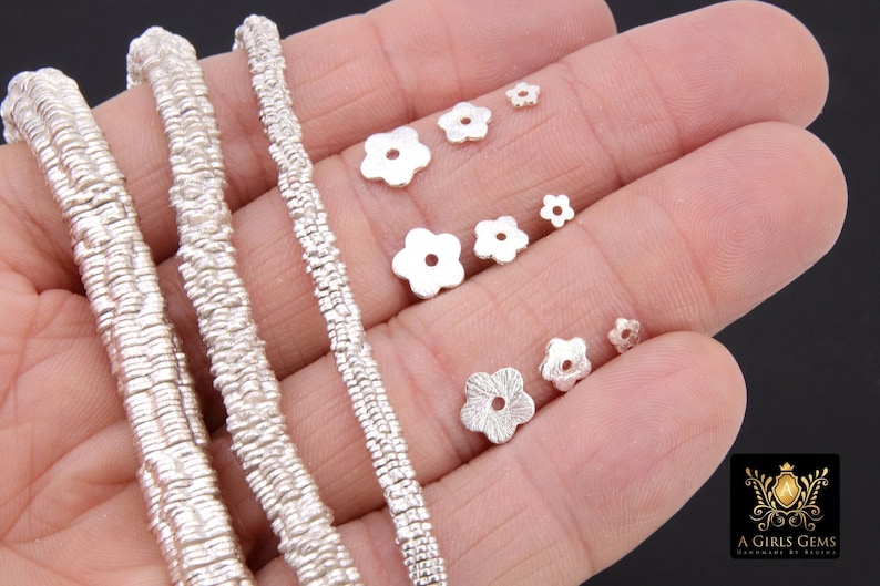 May include: Silver flower-shaped beads in various sizes, perfect for jewelry making. The beads have a textured surface and a hole in the center for threading.