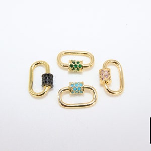 May include: Four gold-colored oval-shaped clasps with decorative center bars. One clasp has a black gem center, another has green gems, a third has turquoise gems, and the last has pink gems. The clasps are on a white background.
