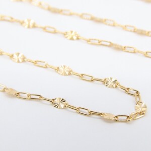 May include: A gold chain necklace with a delicate, patterned design. The chain features small, round links with a textured surface.