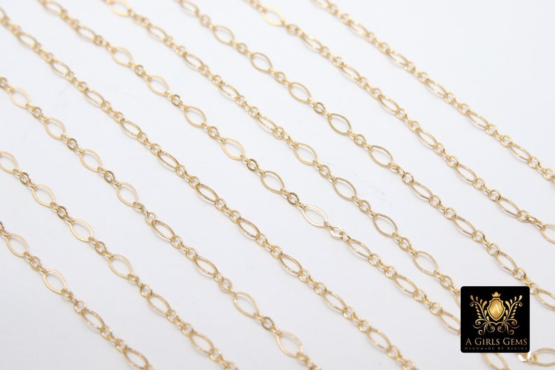 May include: Multiple strands of gold chain, each with a different length, are laid out on a white surface. The chains are made of oval-shaped links.