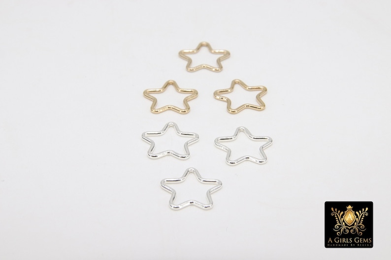 May include: Six star-shaped metal jump rings, three gold and three silver, on a white background.