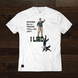 Puede incluir: Camiseta blanca con estampado de camuflaje verde y negro que dice "Remember Sully, I promised to kill you last? I Lied". Una imagen de dibujos animados de un hombre con una camisa verde y pantalones caqui está de pie en el lado izquierdo de la camiseta. Una imagen de dibujos animados de un hombre con traje está cayendo de cabeza en el lado derecho de la camiseta.