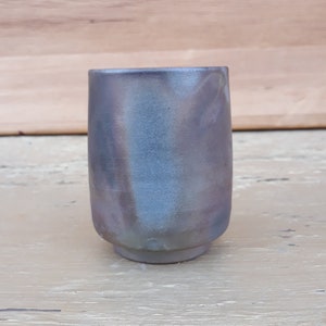 May include: A gray ceramic cup with a subtle iridescent glaze. The cup has a rounded shape and a slightly flared lip.