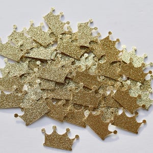 May include: A pile of gold glitter crown confetti. The crowns are scattered on a white background.