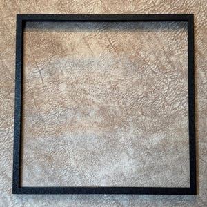 Peut inclure: Un cadre photo carr&eacute; noir avec une surface textur&eacute;e. Le cadre est vide, sans &oelig;uvre d'art ni photo &agrave; l'int&eacute;rieur. Le cadre est fait d'un mat&eacute;riau sombre et a un design simple et moderne.