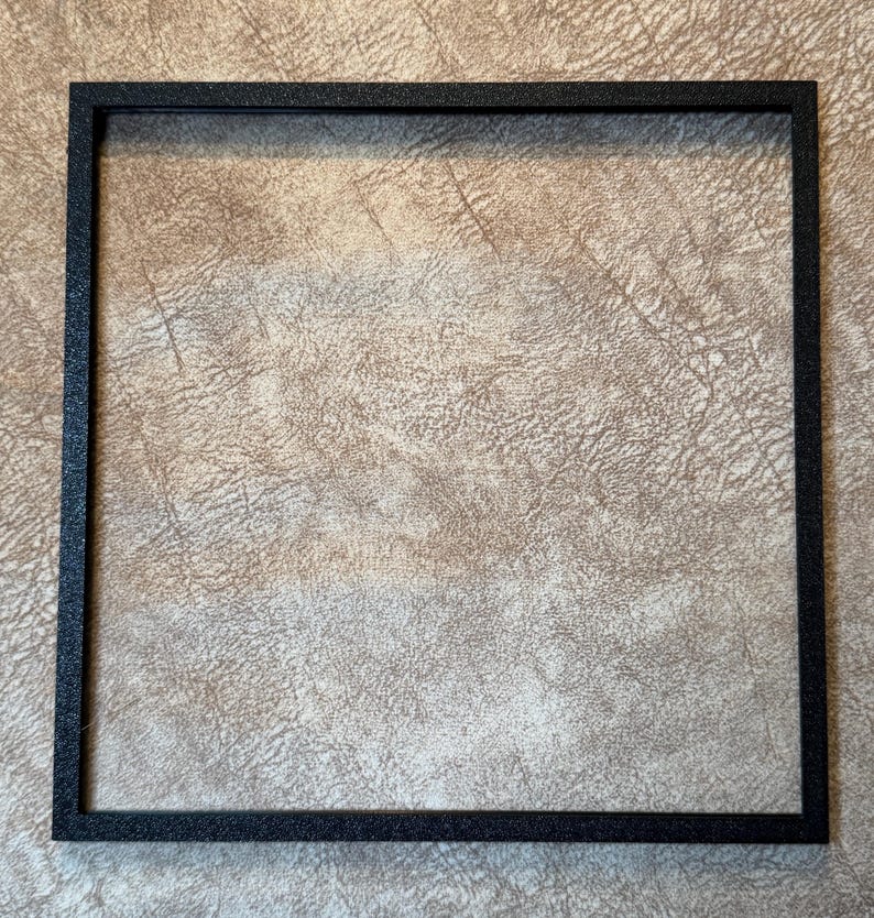 Peut inclure: Un cadre photo carr&eacute; noir avec une surface textur&eacute;e. Le cadre est vide, sans &oelig;uvre d'art ni photo &agrave; l'int&eacute;rieur. Le cadre est fait d'un mat&eacute;riau sombre et a un design simple et moderne.