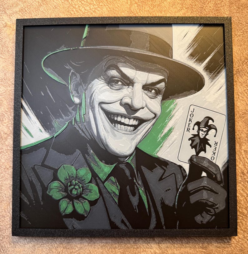 Peut inclure: Impression encadr&eacute;e repr&eacute;sentant le Joker souriant, tenant une carte &agrave; jouer. L'image pr&eacute;sente le Joker en costume et chapeau, avec des d&eacute;tails verts et noirs. La carte indique "Joker". L'impression est dans un cadre noir.