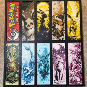 May include: A set of ten rectangular art prints featuring various Pokémon characters. The prints are set in a black frame. The top left print has the Pokémon logo and the text "Gotta catch 'em all!". The other prints feature Eevee and its evolutions.