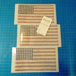 May include: Three sheets of clear adhesive-backed paper with a red, white, and blue American flag design made of small, colorful rhinestones. The rhinestones are arranged in a grid pattern to form the flag.