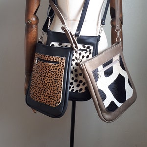 Op de afbeelding: Drie crossbody-tassen met verschillende dierenprintpatronen. De tassen zijn zwart, bruin en grijs met witte accenten. De tassen hangen aan een houten mannequin.