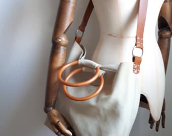 May include: A beige canvas tote bag with two large brown leather rings for handles. The bag has a long brown leather strap.
