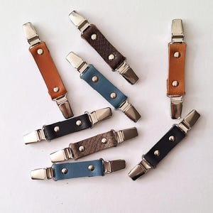 Peut inclure: Sept pinces à vêtements en cuir et métal de différentes couleurs, dont le marron, le noir, le gris et le bleu. Les pinces sont conçues pour maintenir le tissu ensemble.