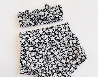 Può includere: Un cerchietto e pantaloncini coordinati con stampa floreale bianco e nero. Il cerchietto è legato con un fiocco. I pantaloncini hanno un orlo arricciato.