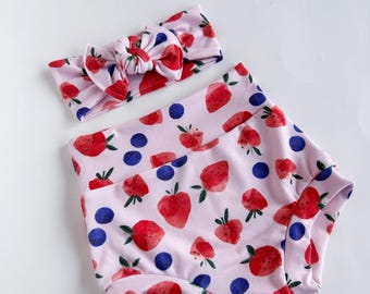 May include: A pink and white headband with a bow and a pair of pink and white bloomers with a strawberry and blueberry print.
