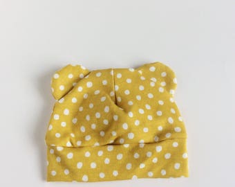 May include: A yellow baby hat with white polka dots and bear ears.