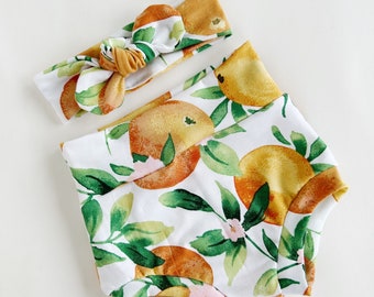 May include: A white and yellow baby bloomer with a watercolor orange and leaf print. A matching yellow headband with a knotted bow is included.