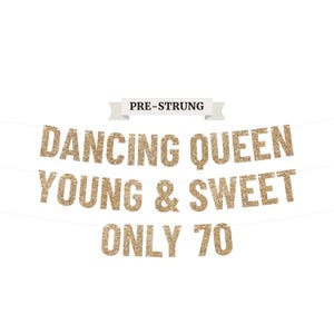 May include: A gold glitter banner with the words "DANCING QUEEN YOUNG & SWEET ONLY 70" strung across a white background. The banner also has the text "PRE-STRUNG" in a banner above the main text.