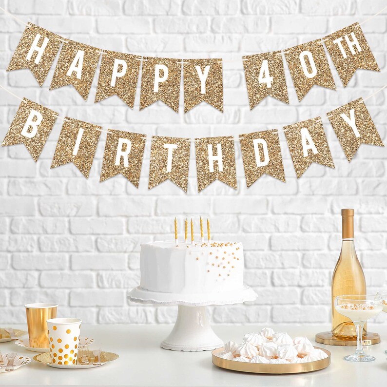 Gold glitter banner with the text "Happy 40th Birthday". A white cake with gold sprinkles sits on a white cake stand. A bottle of wine and a plate of white meringue cookies are on a table.