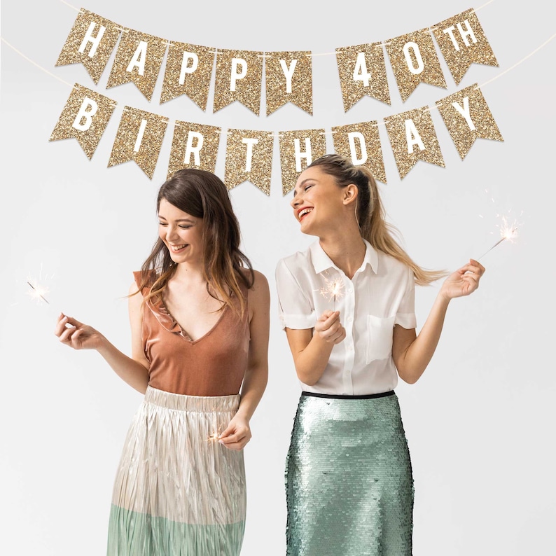 Two friends celebrating a 40th birthday with gold glitter banners that read "Happy 40th Birthday" and sparklers.
