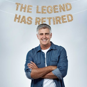 A man in a blue denim shirt with his arms crossed, smiling at the camera. A gold glitter banner above him reads "The Legend Has Retired."